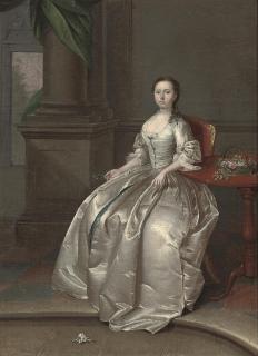 Arthur Devis - Portrait of a lady, seated, full-length, in a white dress, beside a table with a basket of flowers, a sprig of orange blossom in her right hand, in an interior