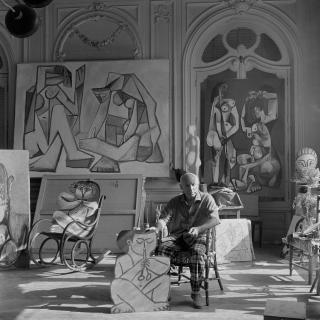 Edward Quinn - \'Pablo Picasso Holding A Cutout Figure Of A Faun, With Another Faun \'Seated\' On The Rocking Chair. Behind Pablo Picasso, Two Paintings Done In 1956. La Californie, Cannes\', 1956