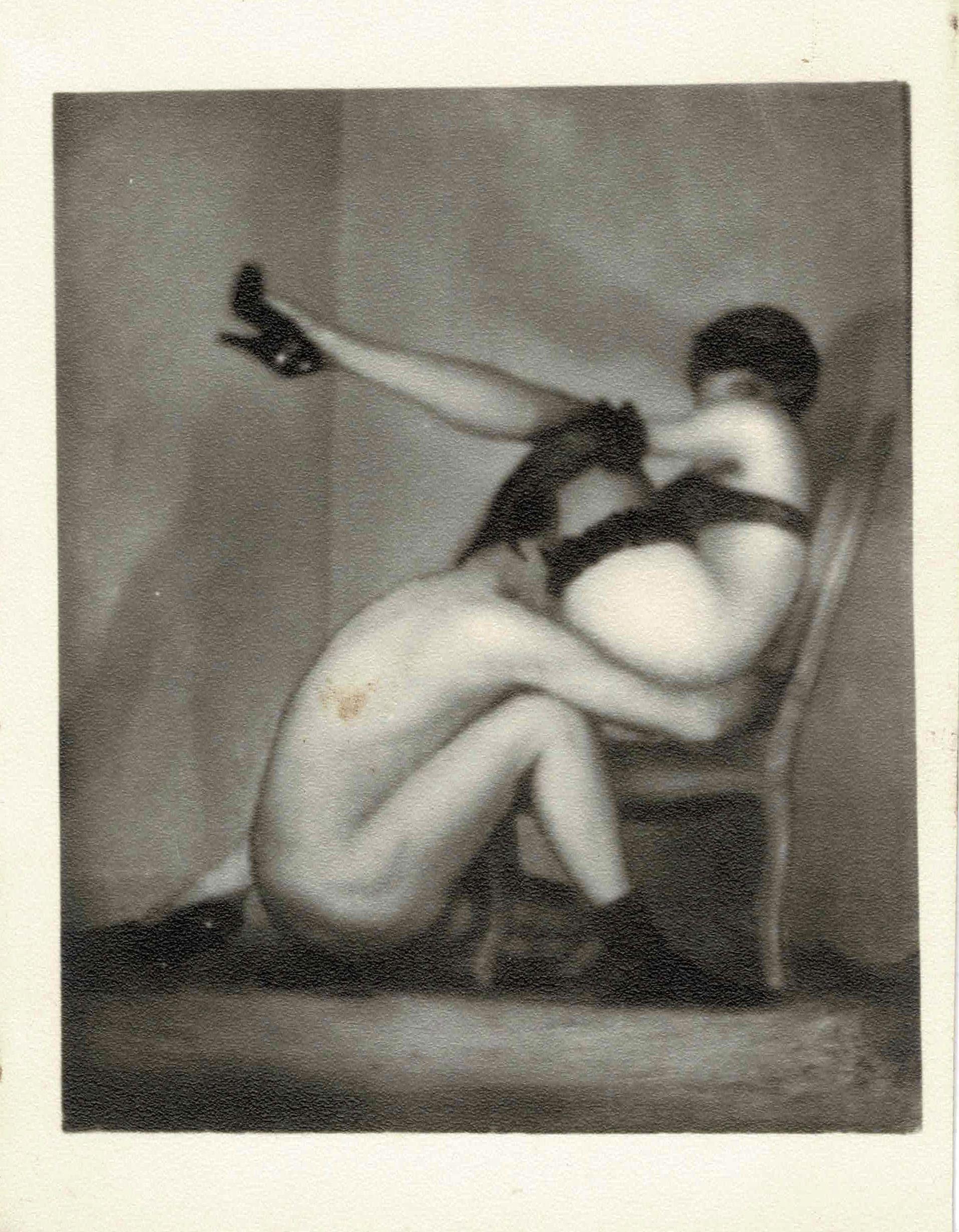 Pierre Molinier - Autoportrait assis par terre pratiquant une fellation sur son double féminin, assis sur une chaise, jambe gauche levée.