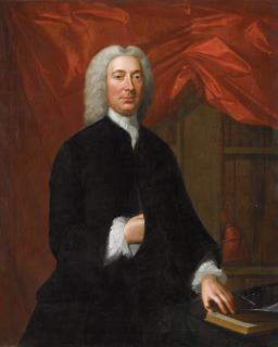 William Verelst - Portrait of a gentleman, three-quarter length, wearing black, with a white cravat, standing beside a table before a red curtain